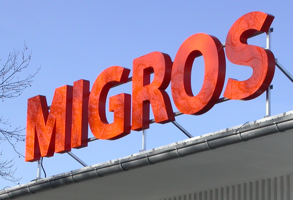 De grandes lettres orange « Migros » sur le toit d’un magasin. 