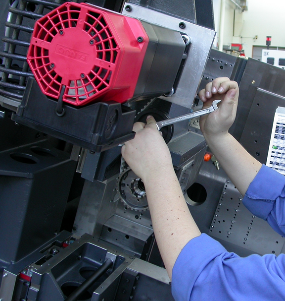 Eine Person zieht mit einem Schraubenschlüssel ein Bauteil an einer industriellen Maschine fest. Ein rotes Motorgehäuse ist vorne an der Maschine montiert.