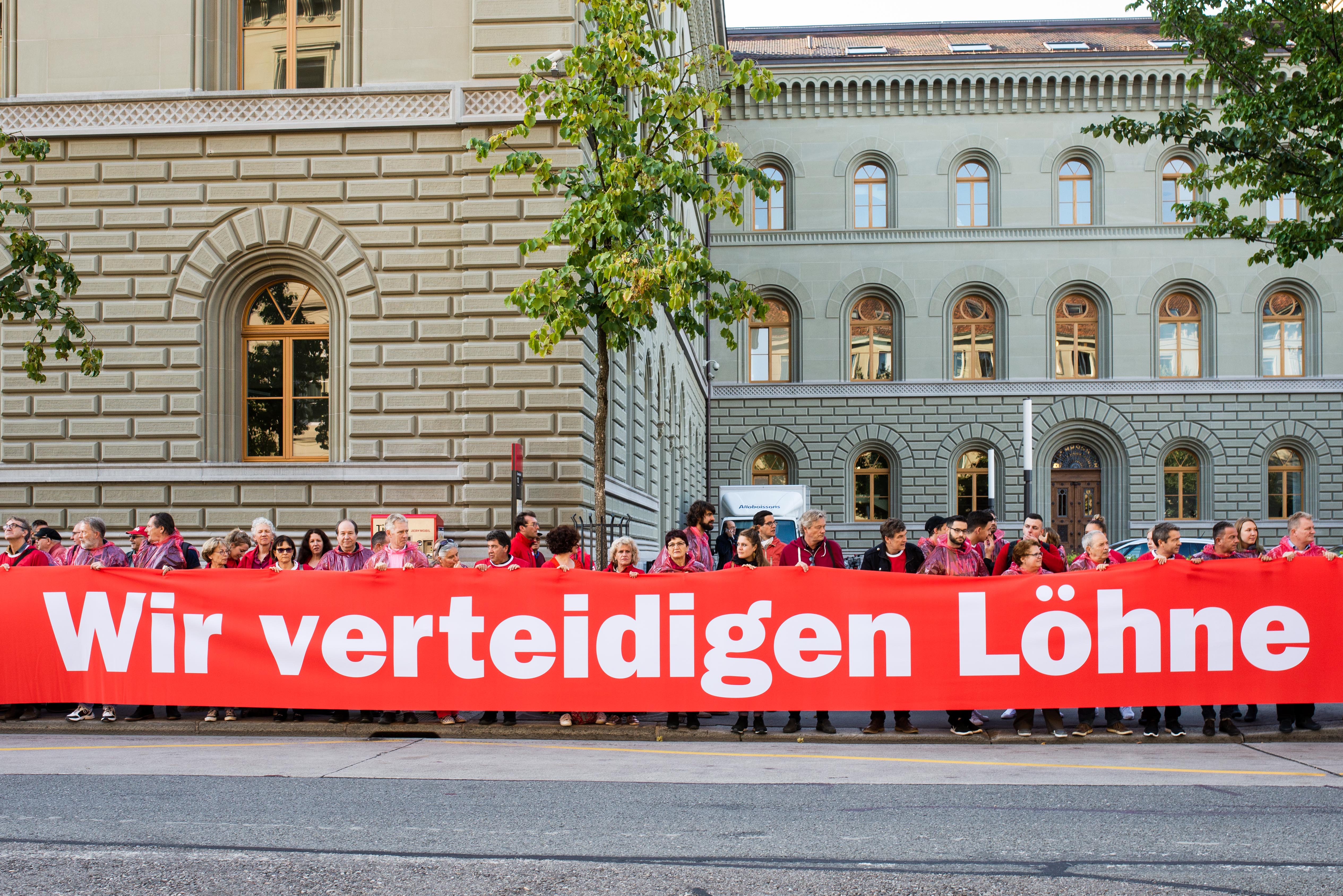 Unia-Aktivist:innen tragen ein Transparent in der Form einer roten Linie für den Lohnschutz.