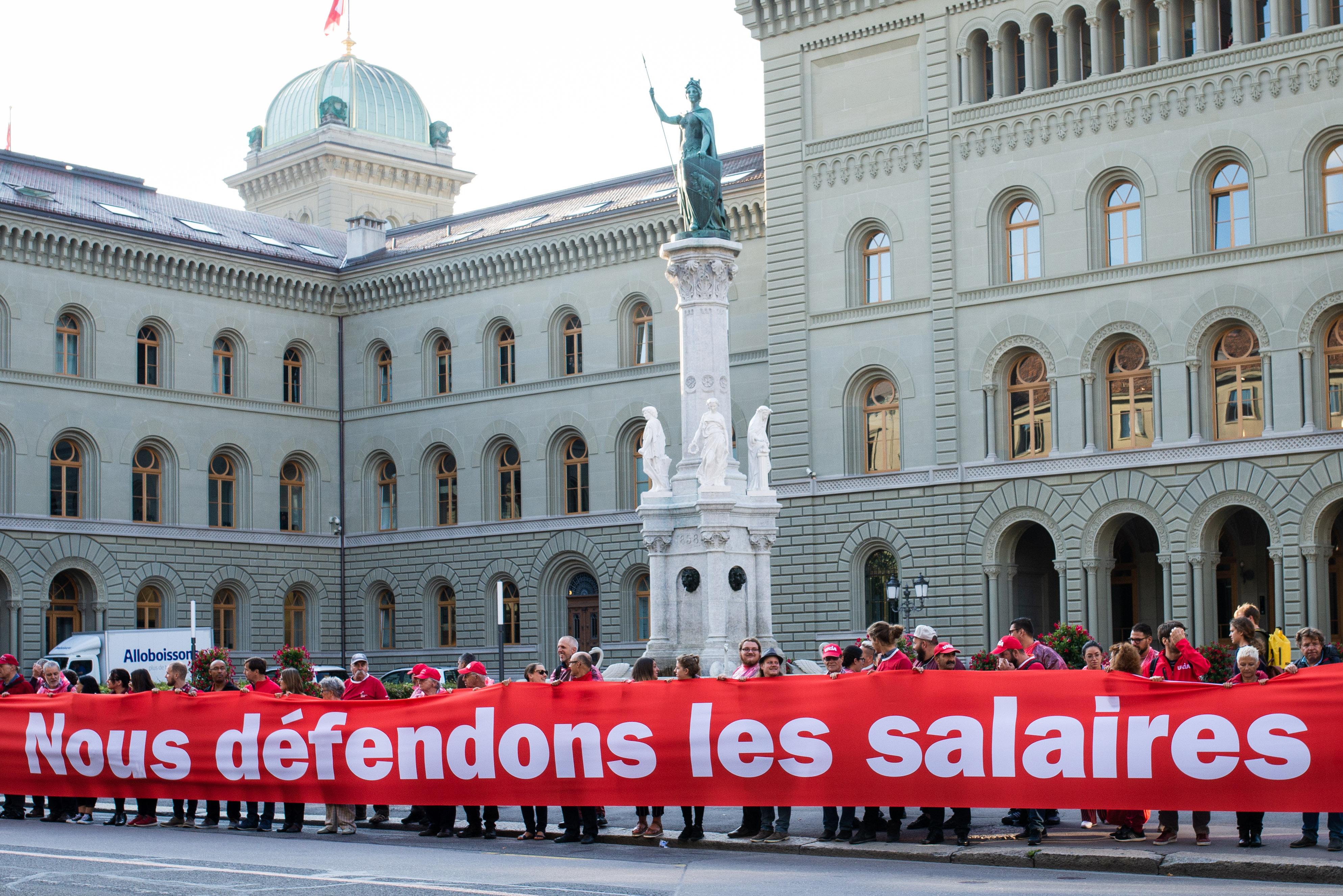 Des personnes tiennent une longue banderole près de la place fédérale à Berne avec les mots « Nous défendons les salaires ».