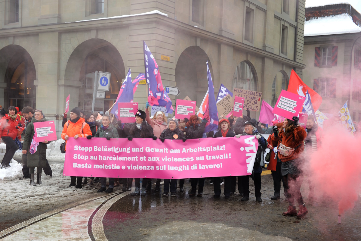 Des femmes d'Unia manifestent sous la neige à Berne. Elles tiennent une grande banderole rose sur laquelle on peut lire «Stop au harcèlement et à la violence au travail» en trois langues.