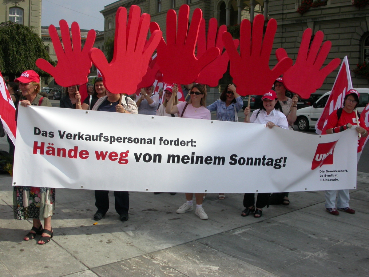 Demonstrantinnen halten einem Transparent mit der Schrift "Das verkaufspersonal fordert: Hände weg von meinem Sonntag!"