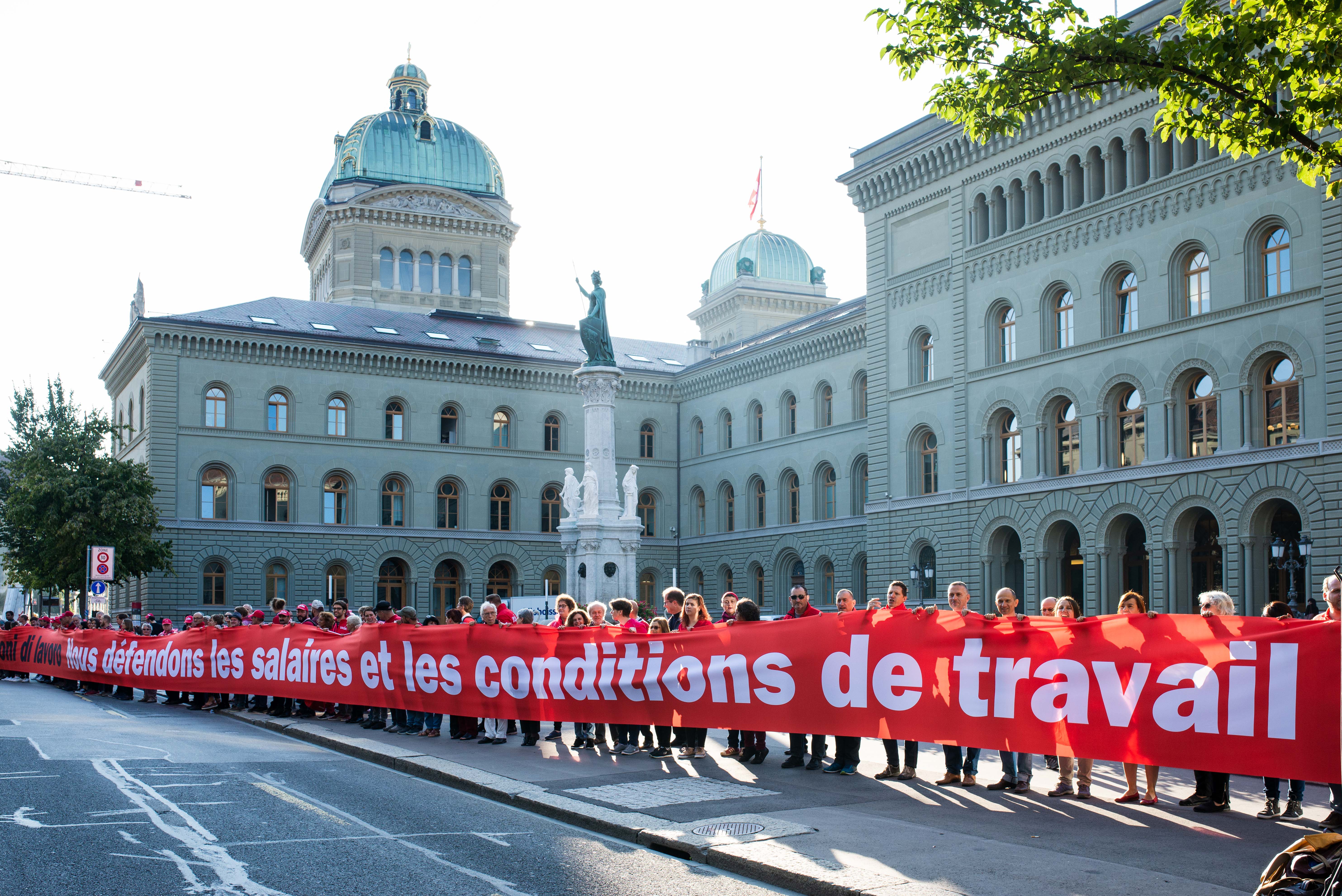 Des gens tracent la ligne rouge devant le Palais fédéral avec une banderole