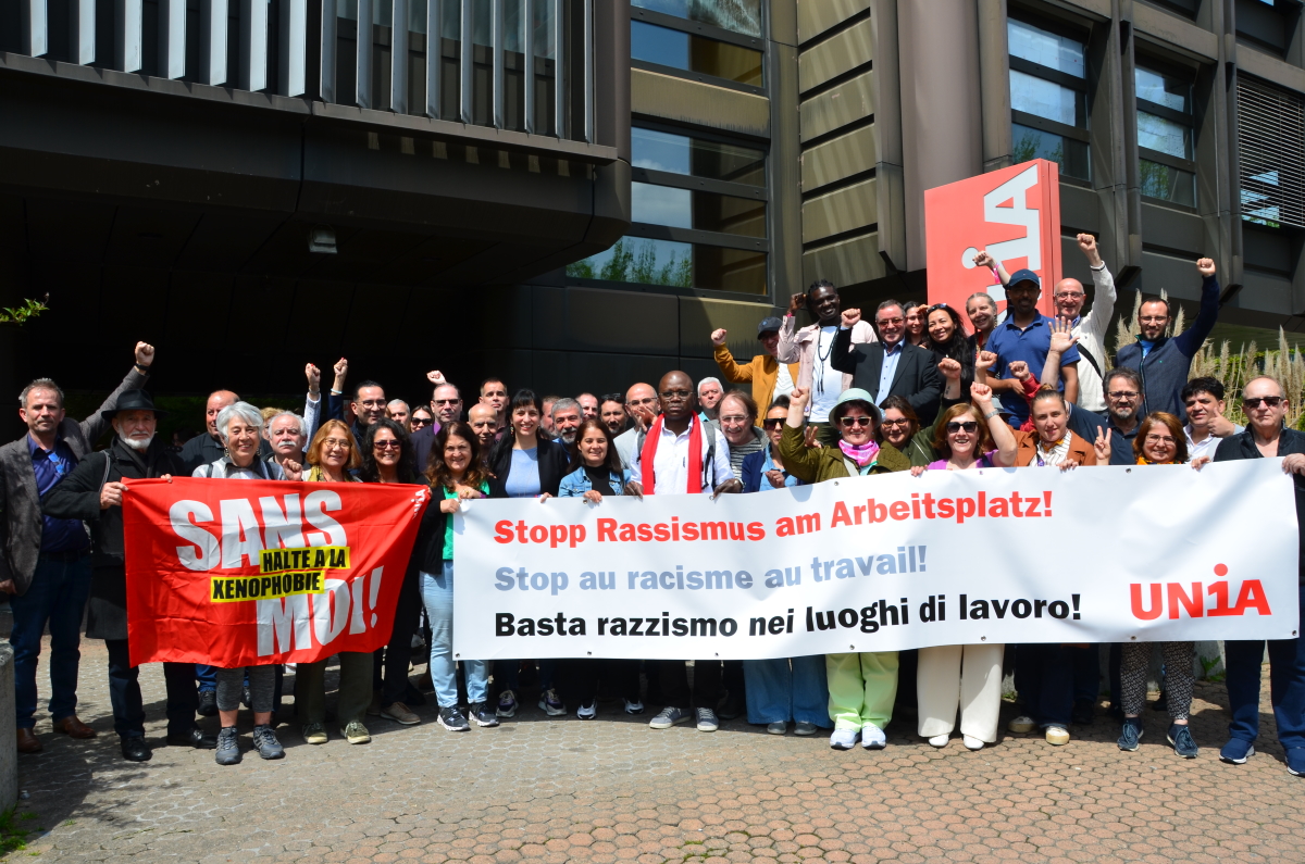 Delegierte der Unia-Migrationskonferenz hinter einem Transparent mit dem Ausdruck "Stopp Rassismus am Arbeitsplatz!"