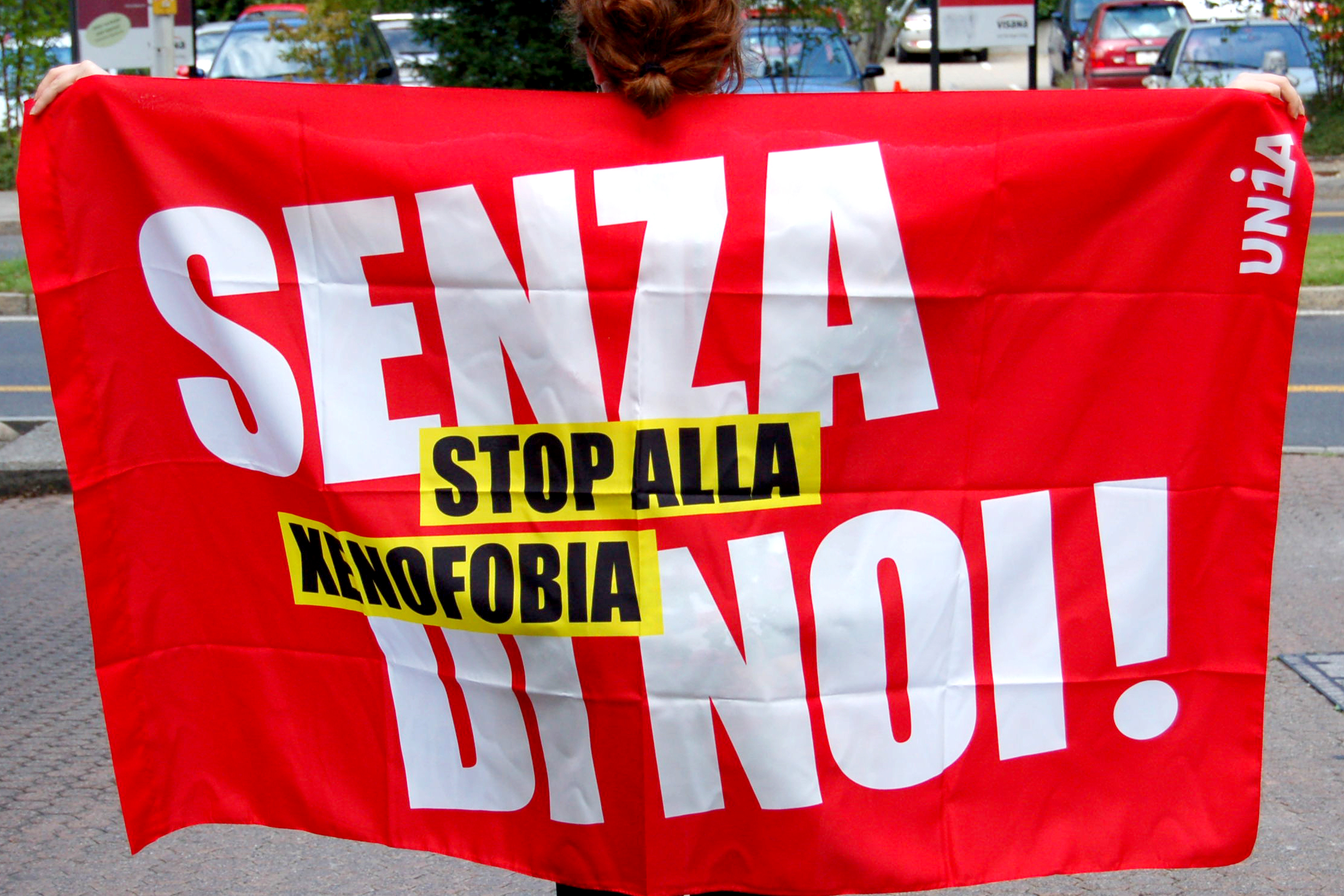 Una donna porta una bandiera sulle spalle: "Senza di noi! Stop alla xenofobia"