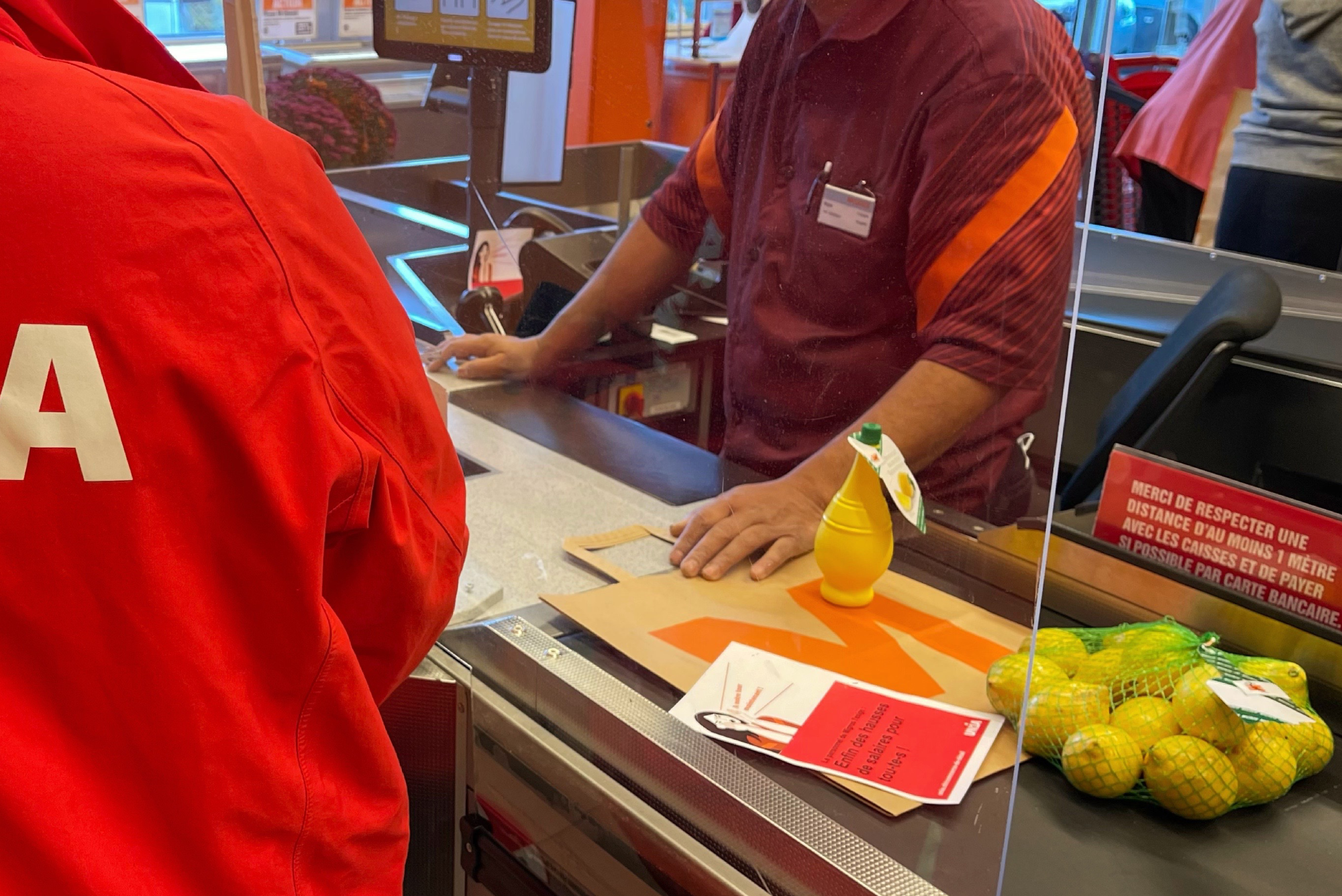 Eine Person mit Unia-Jacke spricht an einer Supermarktkasse mit einem Mitarbeiter.