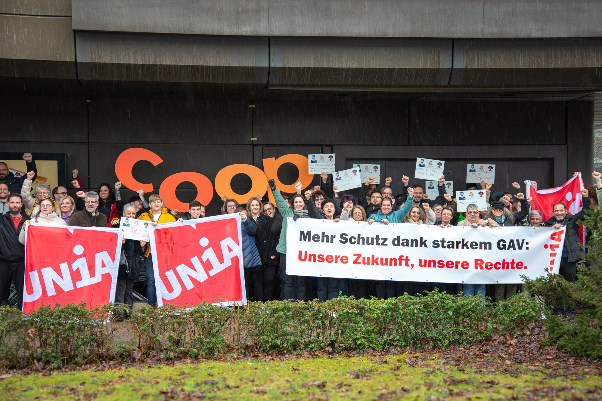 Eine Gruppe Unia-Mitglieder, die bei Coop arbeiten, stehen hinter einem Transparent. Darauf steht «Mehr Schutz dank starkem GAV: Unsere Zukunft, unsere Rechte.». Sie halten Schilder mit Forderungen in die Höhe.