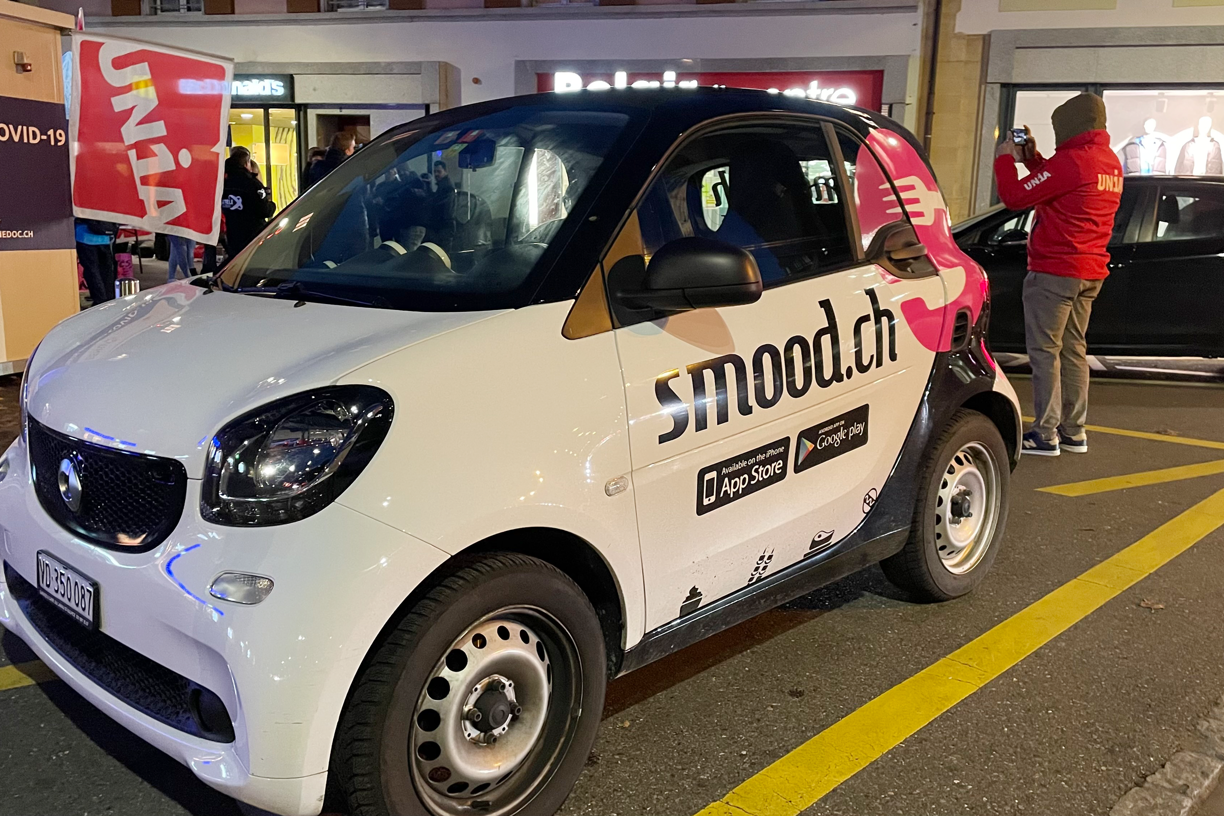 Ein Lieferauto mit der Aufschrift smood.ch, ein Gewerkschaftssekretär in Unia-Jacke und ein Unia-Fahne